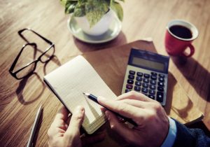 writing in notebook with glasses and calculator on desk