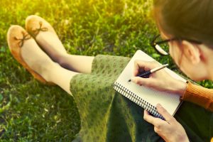 woman sat on grass drawing on a notebook