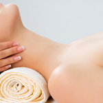 female receiving a neck massage, while her head rests on a rolled up towel